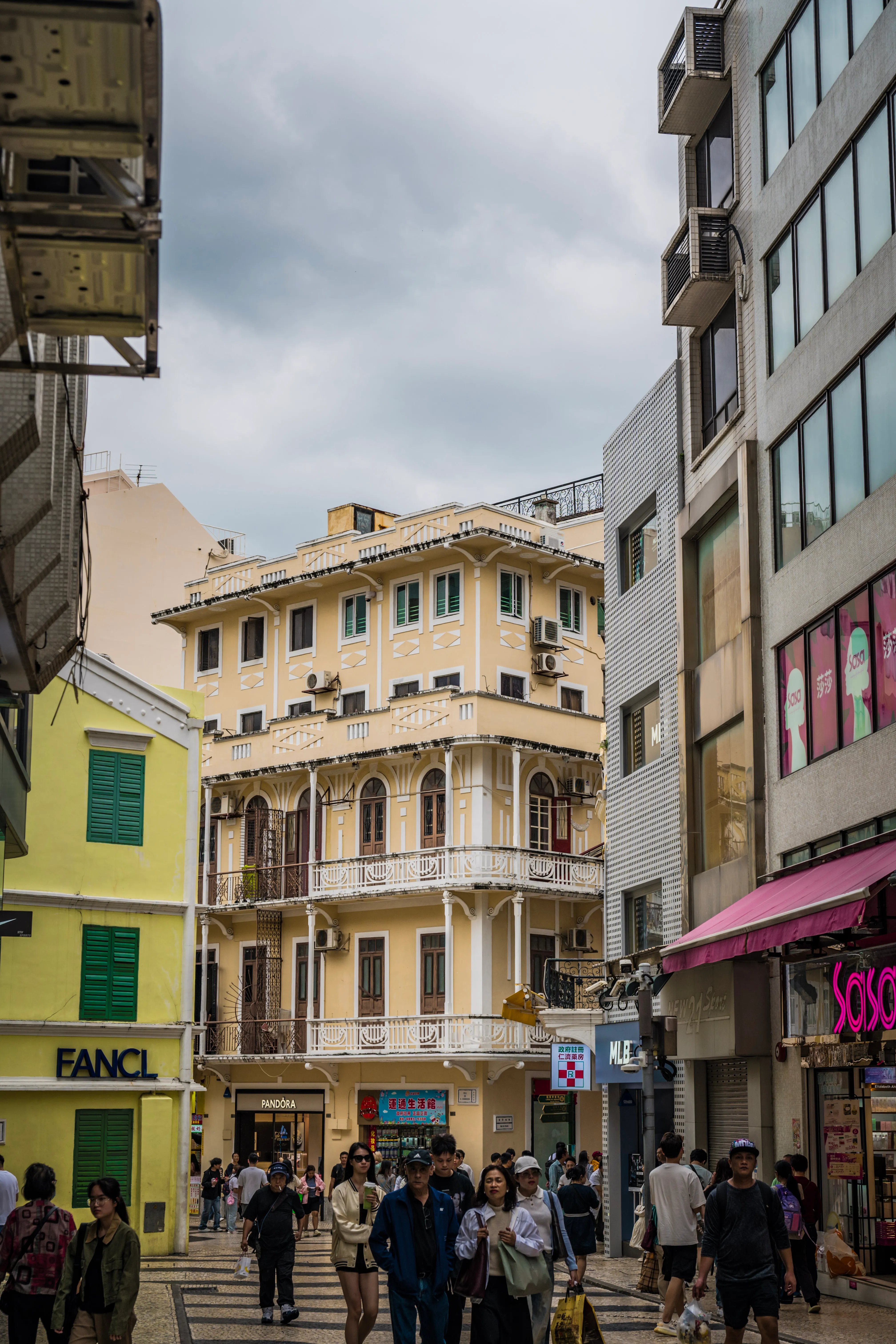 Le passé portugais de Macao, entre néons et vitrines modernes. Des façades pastel aux volets verts et balcons ouvragés dans une rue animée